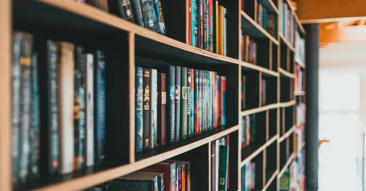 Livres colorés soigneusement rangés sur des étagères modernes dans une bibliothèque lumineuse.