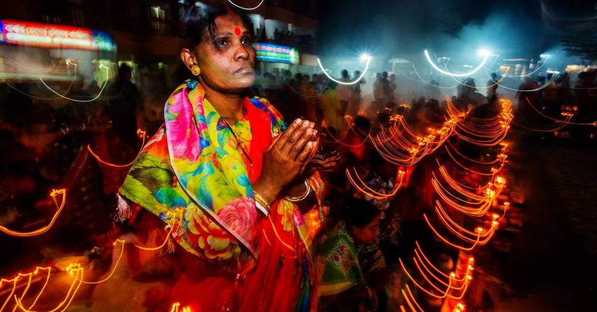 Une femme indienne prie parmi les lumières vives du festival pendant une célébration nocturne.