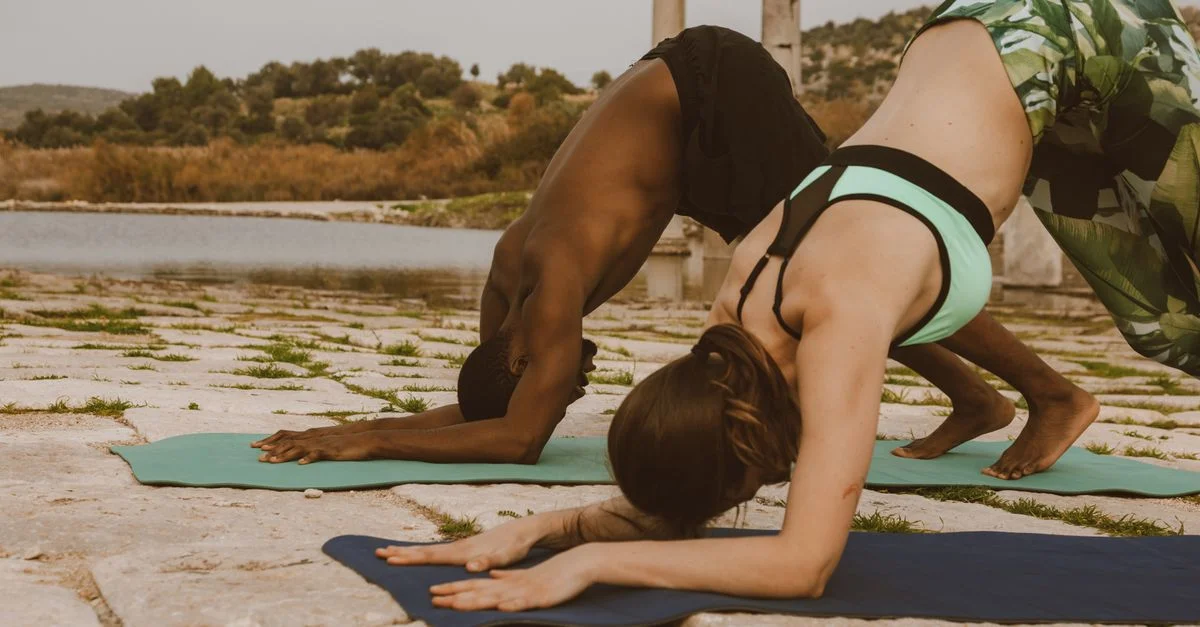 Deux adultes pratiquant le yoga en extérieur sur des tapis, mettant l'accent sur la forme physique et la relaxation.