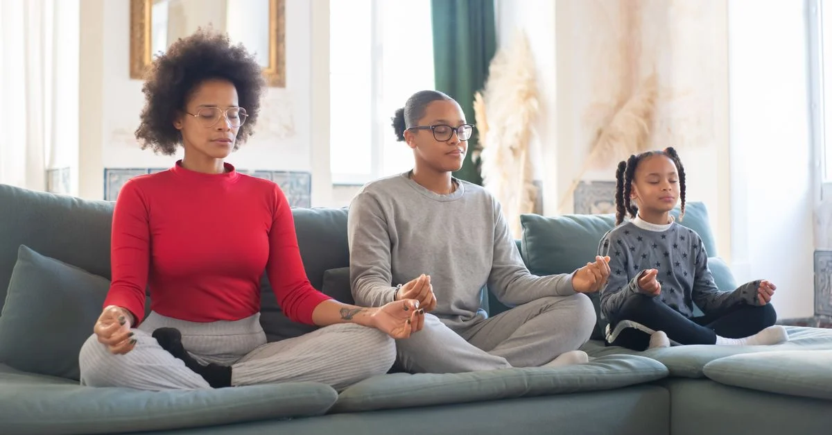 Une mère et ses filles méditent ensemble sur un canapé, embrassant la détente et la pleine conscience à l'intérieur.