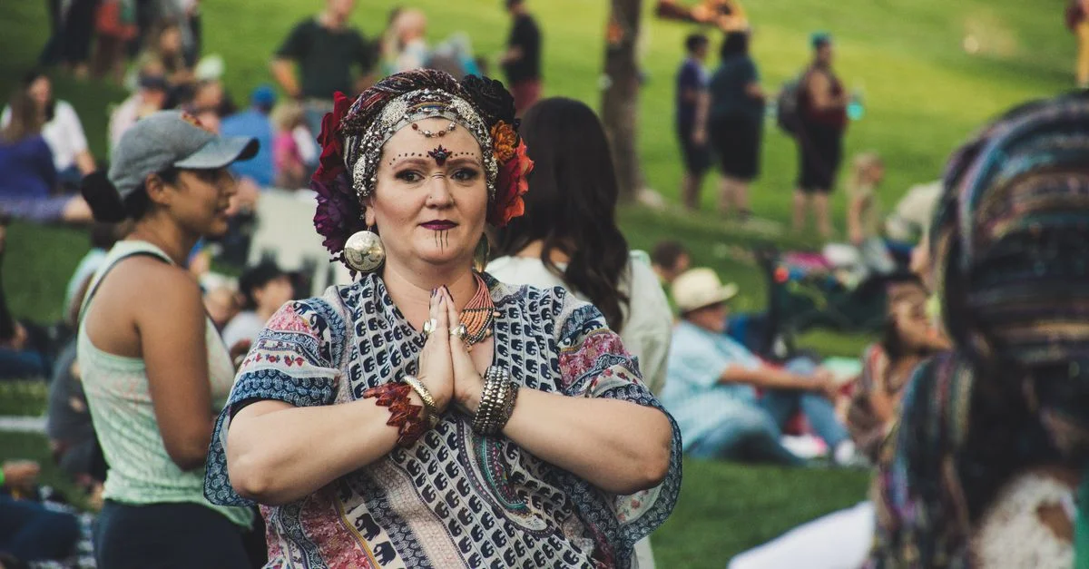 Une femme vêtue d'un habit traditionnel avec du maquillage sur le visage, lors d'un festival animé en plein air dans un parc.